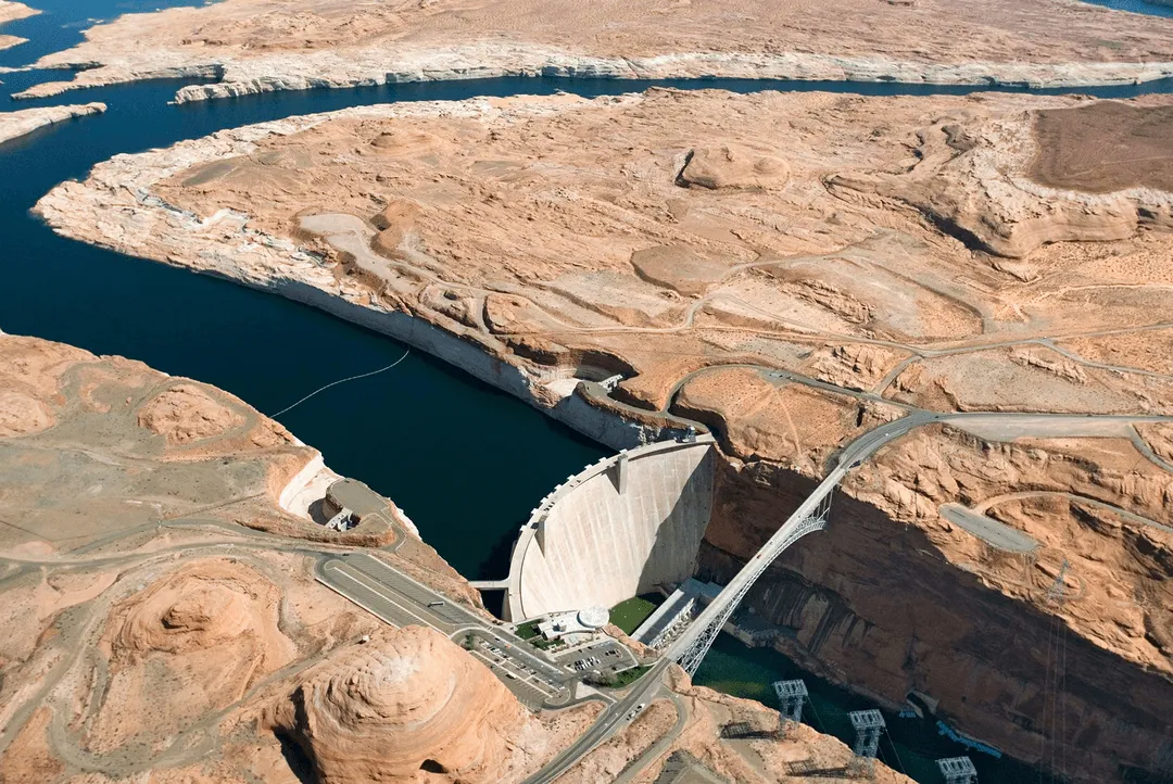 Aerial view of a large concrete dam spanning a deep river canyon with a bridge crossing it.