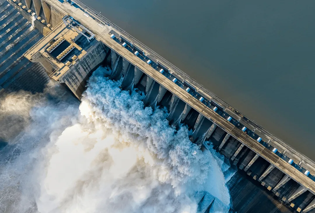 Aerial view of a large dam releasing a massive flow of water into the river below.
